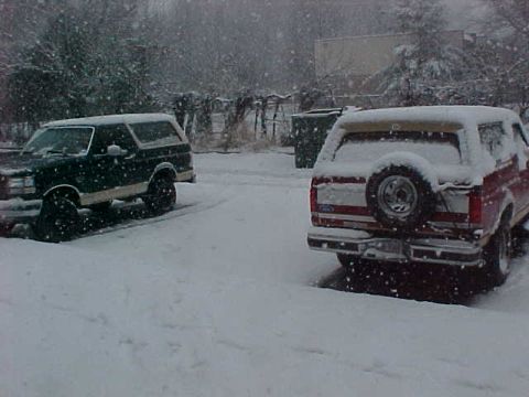 1990 Ford Bronco - Two SUVs are parked in a snowy landscape during a snowfall.