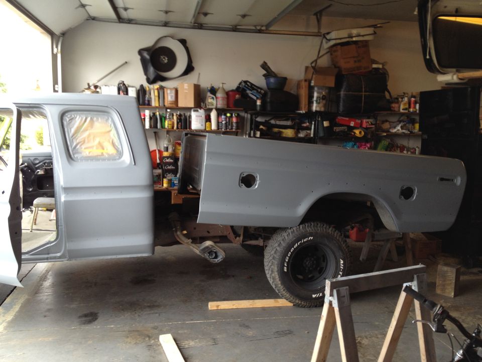 Gray Ford F-Series truck cab and bed in a garage, undergoing disassembly. The windows are covered with plastic