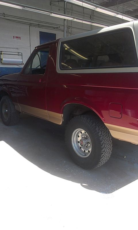 1994 Ford Bronco - Side view of a 1994 Ford Bronco in red and tan, parked indoors.