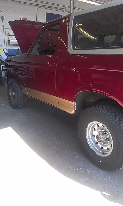 1994 Ford Bronco - Side view of a red Ford Bronco with its hood up, showing the interior and exterior.