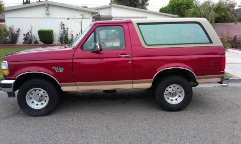 1994 Ford Bronco - This red 1992 Ford Bronco SUV is shown from the side with its tan removable top and tan lower body trim.