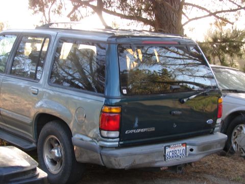 1973 Ford Ranchero - The rear of a two-tone Ford Explorer is visible, parked next to another vehicle under trees.