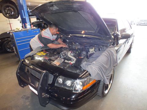 2003 Ford Crown Victoria - Technician works under the open hood of a black Crown Victoria fitted with a front brush guard and forced-induction engine.