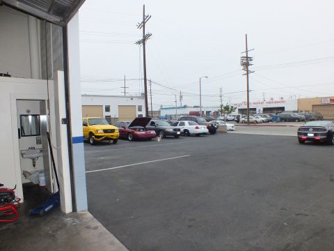 2003 Ford Crown Victoria - View from a shop bay onto a lot of parked cars including a red sedan and white Crown Victoria, with utility poles overhead.