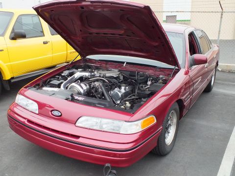 2003 Ford Crown Victoria - Three-quarter front view of a red first-gen Crown Victoria, hood up, supercharger visible in the engine bay.