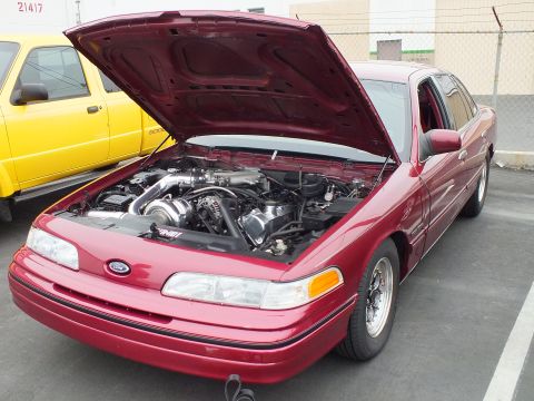 2003 Ford Crown Victoria - Front three-quarter view of a red Crown Victoria with hood open, supercharger and intake piping visible.