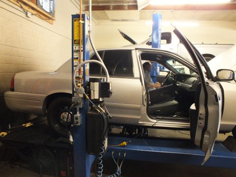 2003 Ford Crown Victoria - Silver Crown Victoria raised on a blue two-post lift with driver door open and a person seated inside.