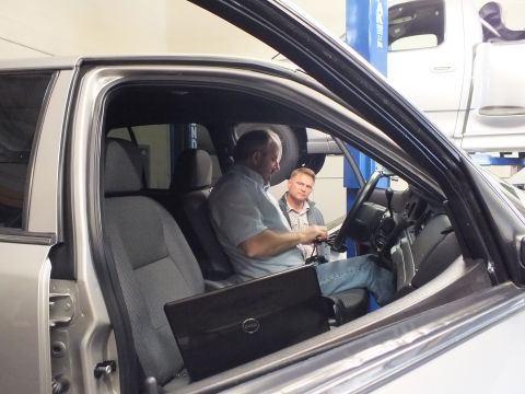 2003 Ford Crown Victoria - Two men sit in the cloth front seats of a silver vehicle with a laptop, viewed through the open passenger door.