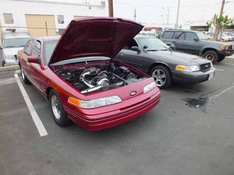 2003 Ford Crown Victoria - Red supercharged Crown Victoria with raised hood parked among a gray Crown Victoria and an SUV in a lot.