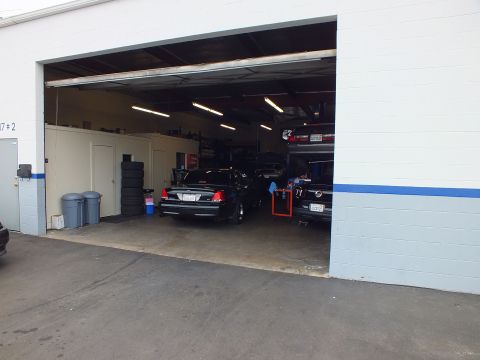 2003 Ford Crown Victoria - View into a repair shop bay through the roll-up door showing a black sedan and stacked tires