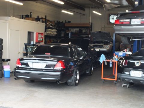 2003 Ford Crown Victoria - Rear three-quarter of a black Crown Victoria in a busy shop bay alongside vehicles on a lift