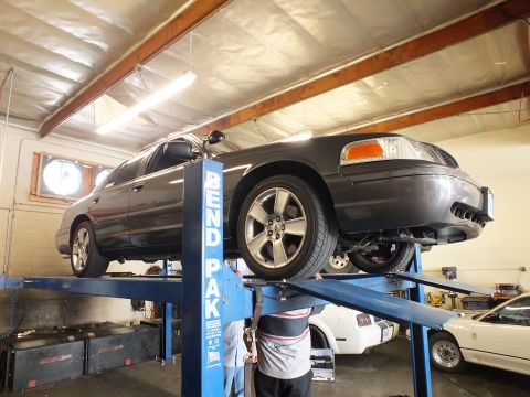 2003 Ford Crown Victoria - Gray luxury sedan lifted on a blue BendPak alignment rack with a technician working underneath
