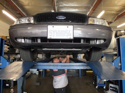 2003 Ford Crown Victoria - Direct front view of a Ford sedan raised on a four-post lift, plate 5YWN854, mechanic beneath it