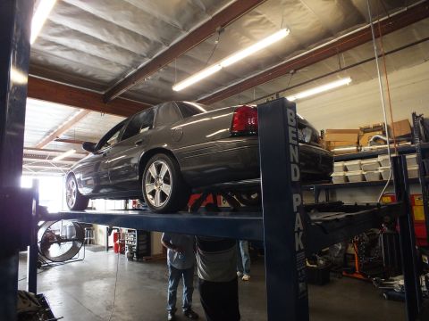 2003 Ford Crown Victoria - Rear three-quarter of a gray sedan on a blue BendPak rack with onlookers at floor level