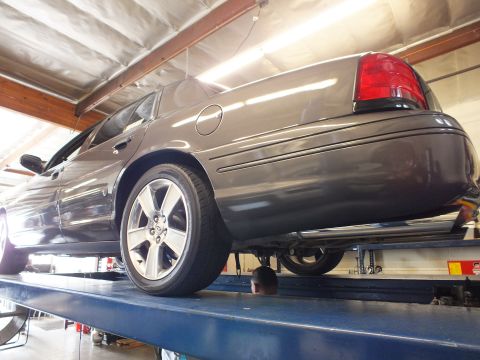 2003 Ford Crown Victoria - Low-angle rear shot of a gray sedan on a shop lift, alloy wheel and red taillight in frame