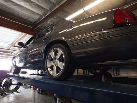 2003 Ford Crown Victoria - Upward angle of a gray sedan elevated on a lift exposing the alloy wheel and rear exhaust