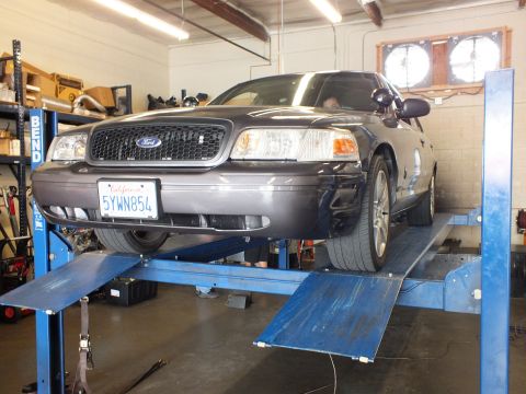 2003 Ford Crown Victoria - Black Ford sedan raised on a blue BendPak rack, Ford grille emblem and California plate 5YWN854 shown