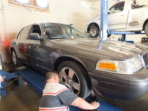 2003 Ford Crown Victoria - Technician inspects the front tire of a gray full-size Ford sedan parked on a shop alignment rack