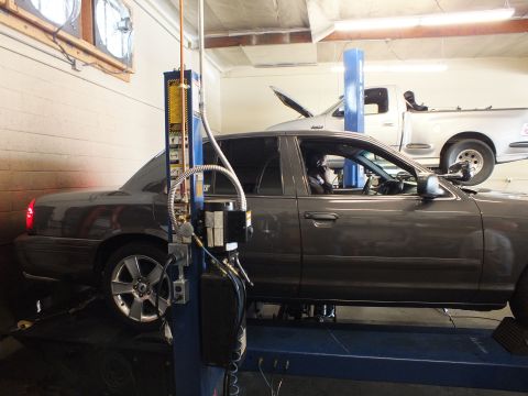 2003 Ford Crown Victoria - Side view of a gray sedan positioned at a hydraulic lift column with alignment equipment attached
