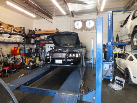 2003 Ford Crown Victoria - Wide shop view of a black sedan with grille guard and raised hood on a four-post alignment rack