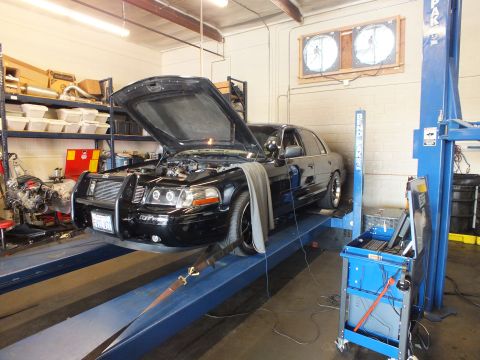 2003 Ford Crown Victoria - Black full-size Ford sedan with front bull bar and open hood undergoing work on a blue rack