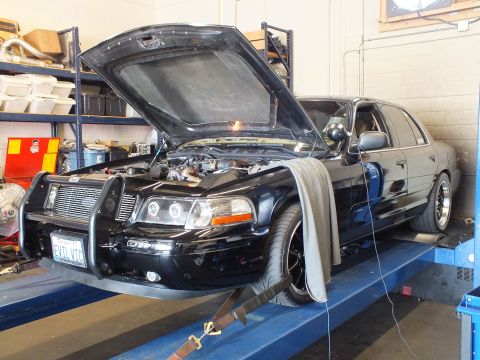 2003 Ford Crown Victoria - Front quarter of a modified black sedan on a rack showing front-mount intercooler and grille guard
