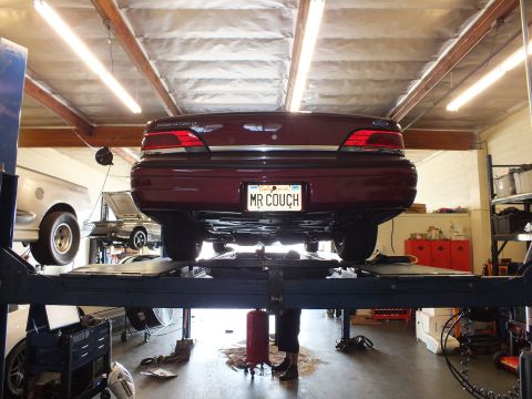 2003 Ford Crown Victoria - Underside rear view of a maroon Ford sedan raised on a four-post lift in a service bay