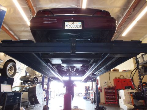 2003 Ford Crown Victoria - Maroon Ford sedan lifted overhead exposing its undercarriage above a busy shop floor