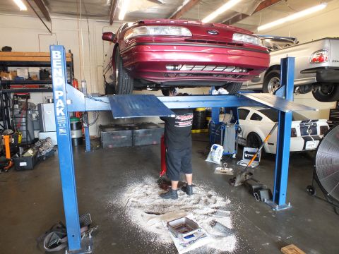 2003 Ford Crown Victoria - Rear view of a maroon Ford sedan raised on a lift while a worker stands underneath in the shop