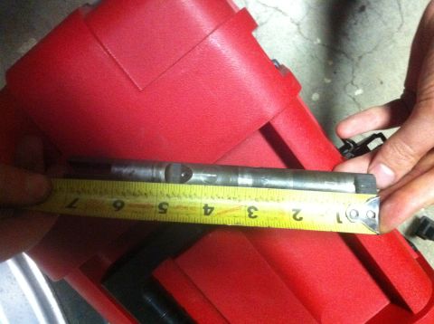 1989 Ford Bronco - A metal shaft is being measured with a yellow tape measure, with a red plastic container in the background.