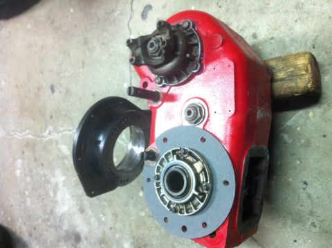 1989 Ford Bronco - A red transfer case housing with a black adapter plate and bearing assembly is shown on a concrete floor.