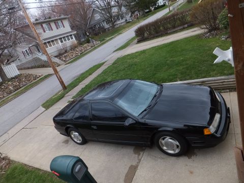 1970 Ford Ranchero - A black coupe with a sunroof is parked on a driveway in front of a residential house.