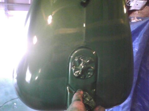 2003 Ford Crown Victoria - A hand is painting a vehicle's fuel tank green in what appears to be a workshop.