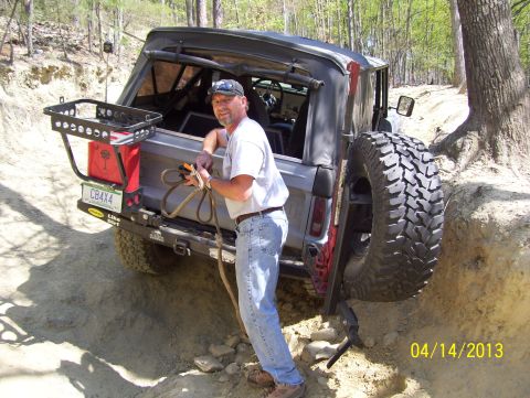 1990 Ford Bronco - A man holds a rope next to a lifted 1990 Ford Bronco on a challenging dirt trail.