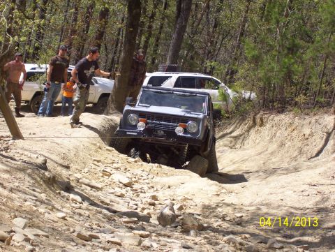 1990 Ford Bronco - Off-road vehicle navigates a challenging dirt path with spectators present.