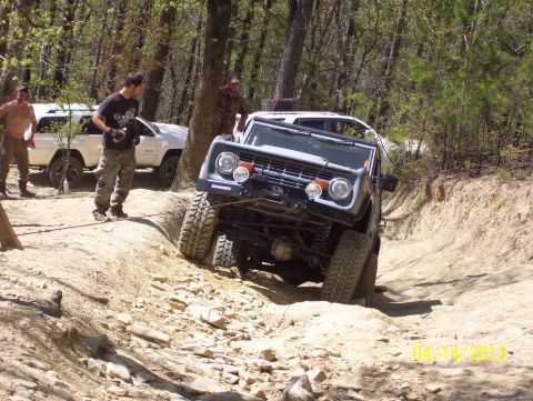1990 Ford Bronco - A dark gray Ford Bronco navigates a challenging off-road trail with another vehicle in the background.