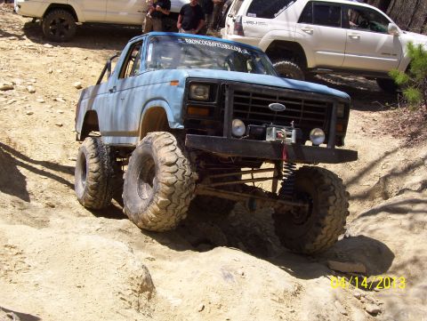 1990 Ford Bronco - This heavily modified 1980 Ford Bronco navigates a challenging off-road course, with other vehicles visible in the background.
