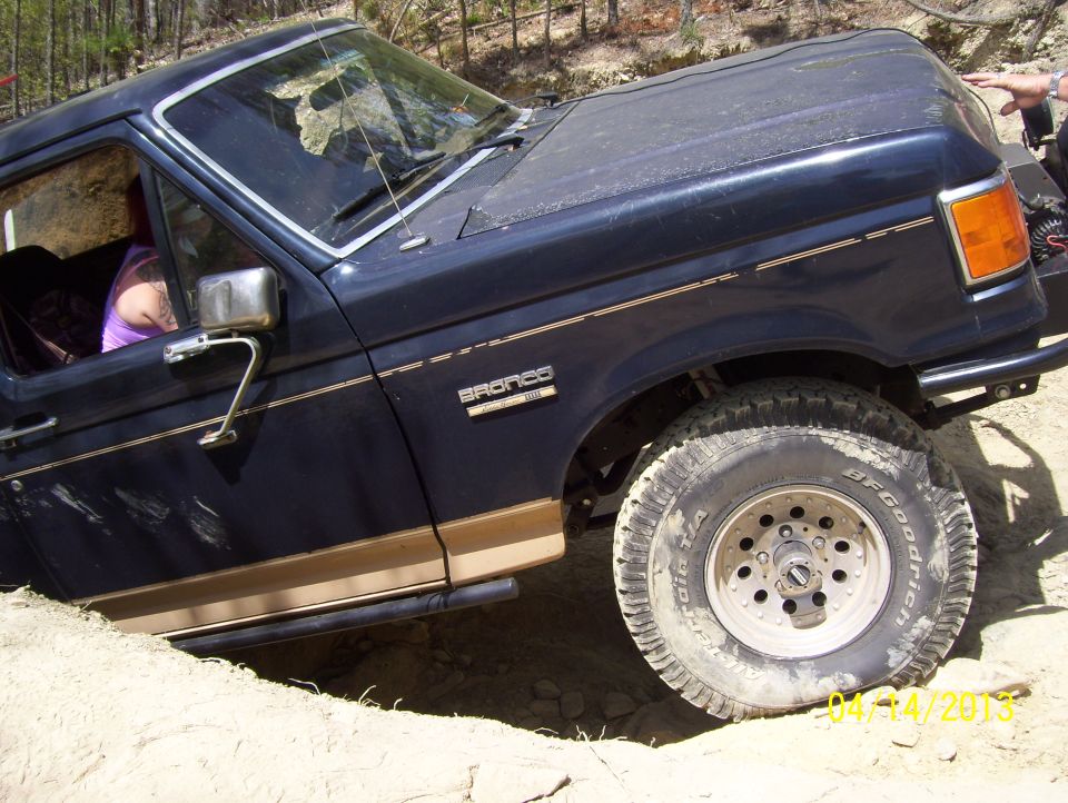 Dark blue Ford Bronco with gold trim, off-roading on a dirt hill. The front passenger side wheel is turned