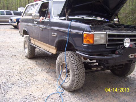 1990 Ford Bronco - 1990 Ford Bronco with hood open, parked outdoors on a gravel surface.