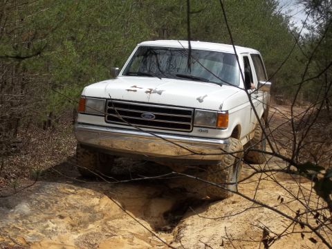 1990 Ford Bronco - This white Ford Bronco II is navigating a rough dirt path surrounded by dense woods.