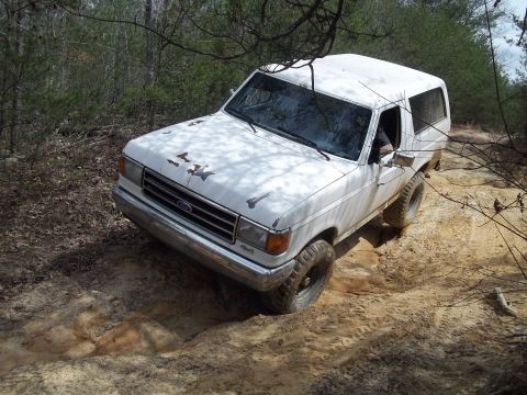 1990 Ford Bronco - A white 1987 Ford Bronco navigates a sandy, wooded trail.
