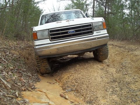 1990 Ford Bronco - A white Ford truck navigates a challenging off-road trail with steep inclines.