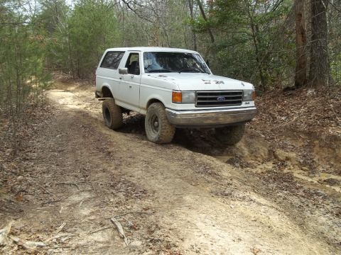 1990 Ford Bronco - This 1990 Ford Bronco navigates a challenging off-road path through a wooded area.