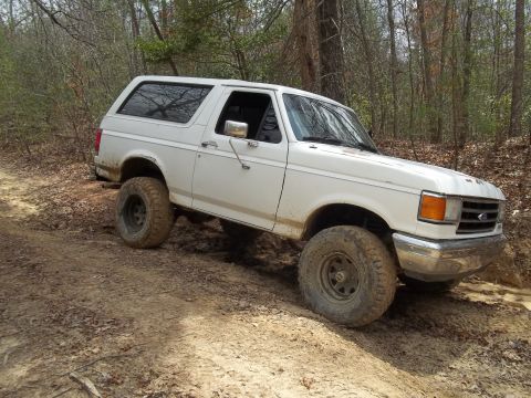 1990 Ford Bronco - 1990 Ford Bronco navigating an off-road trail with large tires.