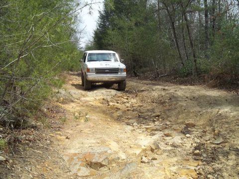 1990 Ford Bronco - White 1990 Ford Bronco navigates a challenging rocky trail through a wooded area.
