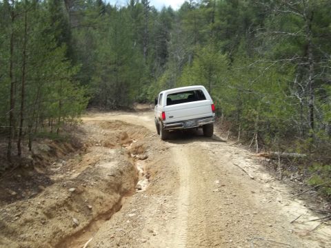 1990 Ford Bronco - White 1990 Ford Bronco navigates a challenging dirt road with visible ruts and erosion.
