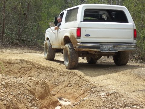 1990 Ford Bronco - A white Ford Bronco navigates a rough dirt path with trees in the background.