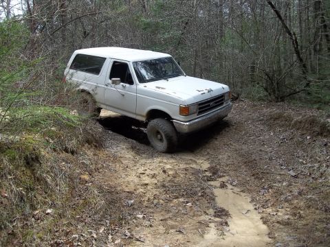 1990 Ford Bronco - This white 1990 Ford Bronco navigates a challenging off-road path through a wooded area.