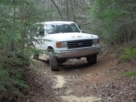 1990 Ford Bronco - A white Ford truck navigates a muddy, wooded trail.