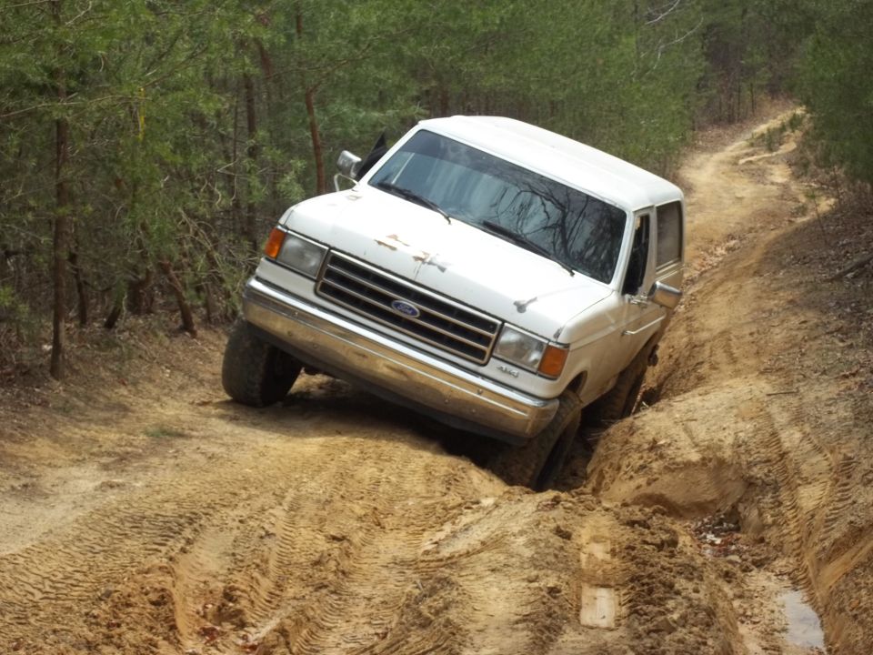 White Ford Bronco on a dirt trail, front-left wheel in a ditch